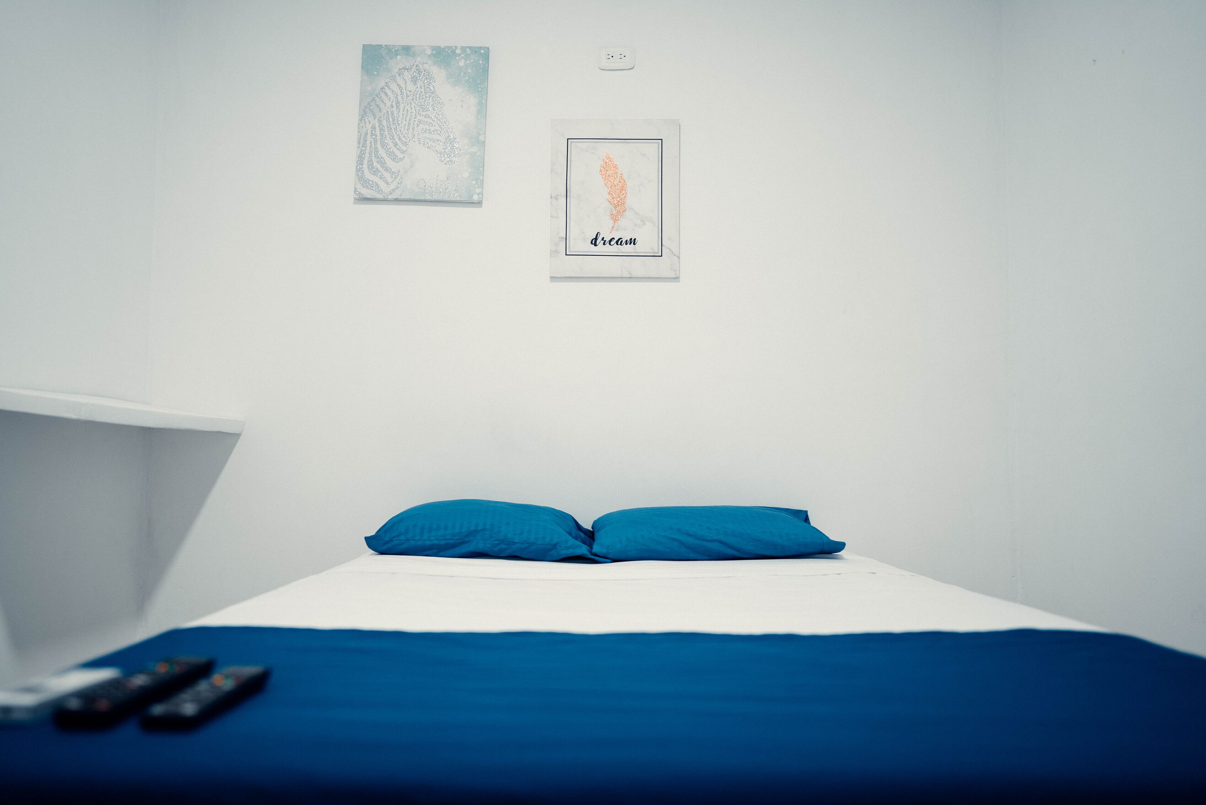 A bedroom with a bed, two pillows, a nightstand, and two remote controls.