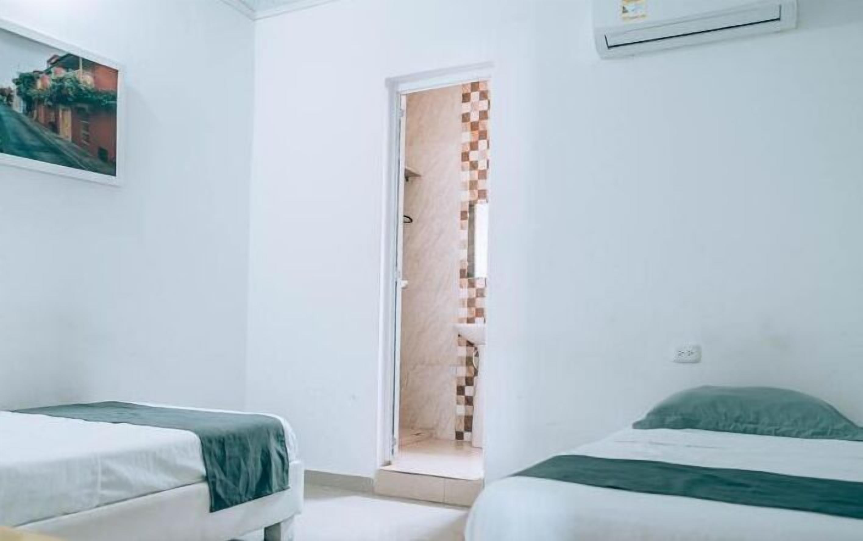 A room with two beds, a painting on the wall, and a door leading to a bathroom with a checkered shower curtain.