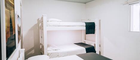 A bunk bed room with white bedding and a window.