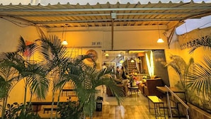Entrada de un hotel con un letrero que dice "HOTEL NEOS", que cuenta con un patio empedrado con asientos al aire libre y plantas en macetas.