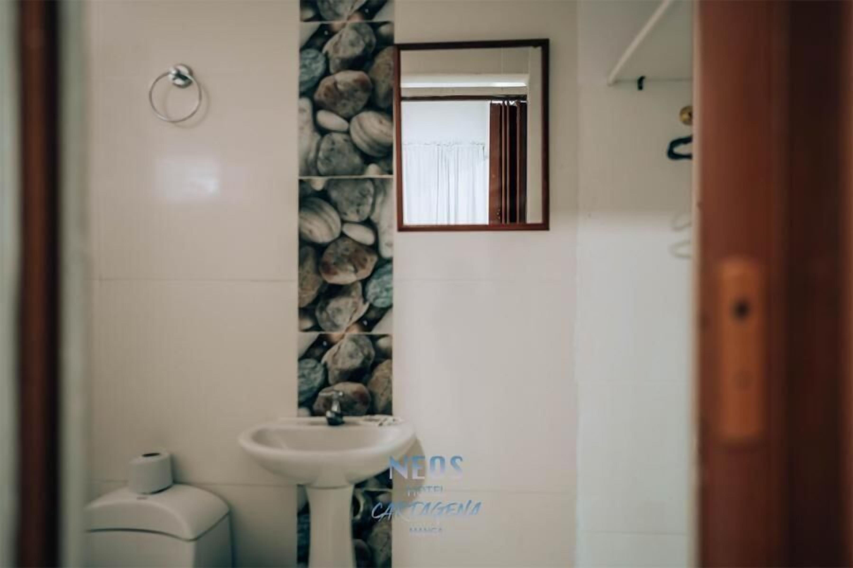 Un baño con lavamanos blanco, un espejo y una pared de piedra.