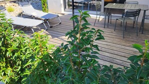 Una terraza de madera con sillones de descanso y una mesa, rodeada de follaje.