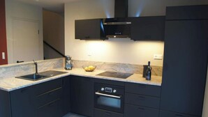 Una cocina moderna con armarios oscuros, horno empotrado, cafetera y un bol de fruta en la encimera.