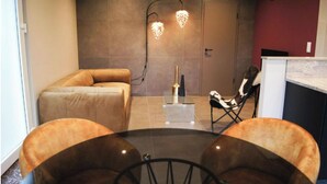Una sala de estar moderna con un sofá, una mesa de comedor y sillas. Hay un aplique decorativo en la pared y una puerta al fondo.