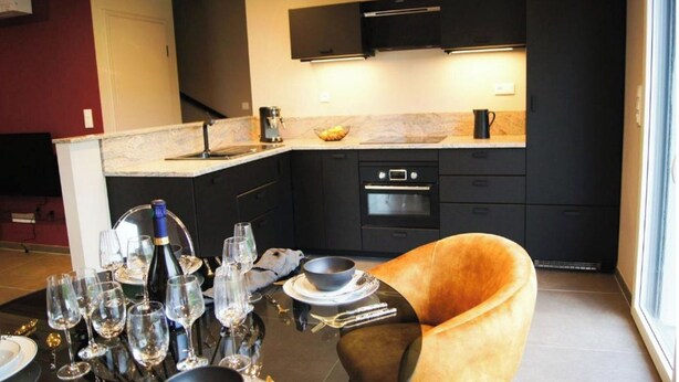 Una cocina moderna con armarios oscuros, horno empotrado y comedor con mesa lista para una comida.