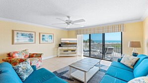 Een woonkamer met een televisie, blauwe banken en een balkon met uitzicht op het strand.