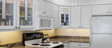 Una cocina con armarios blancos, estufa, microondas y refrigerador.