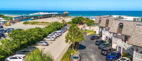 A parking lot with multiple cars, a building with a balcony, and a view of the ocean.