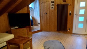 Une pièce mansardée chaleureuse avec des murs en bois, un téléviseur à écran plat, une petite table en bois et un tapis gris.