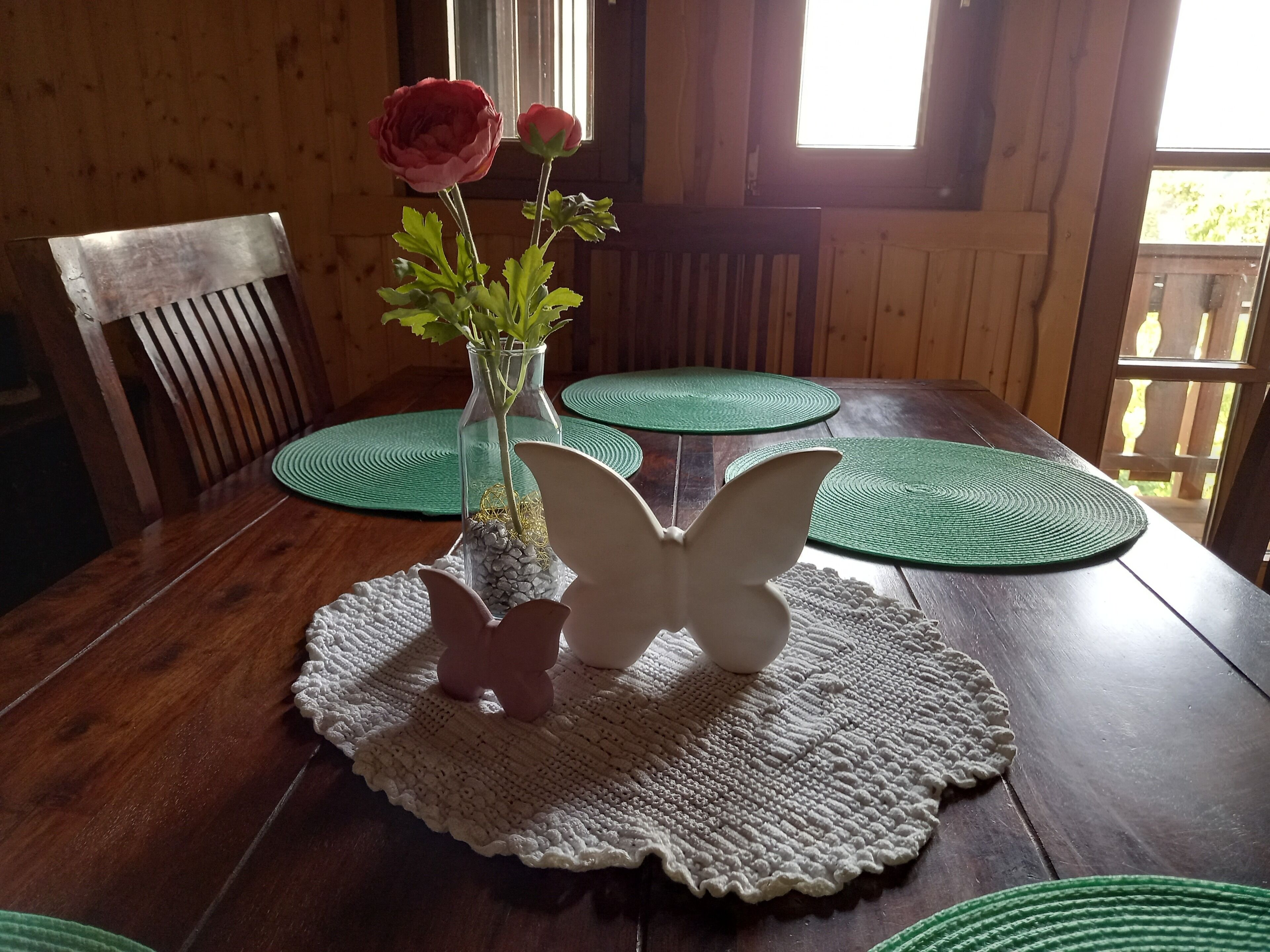 Ein Holztisch mit einer Blumenvase, einem kerzenhalter in Schmetterlingsform und grünen Platzsets.