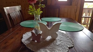 Une table de salle à manger en bois, ornée d’un vase de fleurs, d’un chandelier en forme de papillon et de sets de table verts.
