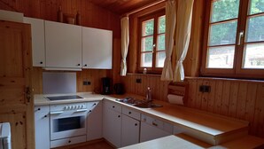 Une cuisine rustique dans une cabane en bois, avec des meubles blancs, une cuisinière Bosch, un évier et une fenêtre agrémentée de rideaux.