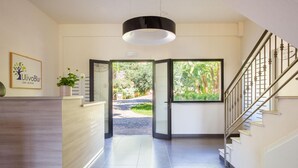 Ein Hotel-Rezeptionsbereich mit einem Holzbüro, einer großen Pendelleuchte und Blick auf den Garten durch eine Glastür.