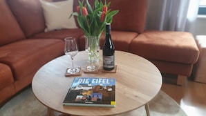 Ein runder Holztisch mit einer Zeitschrift, einer Weinflasche und einem Weinglas auf Untersetzern.