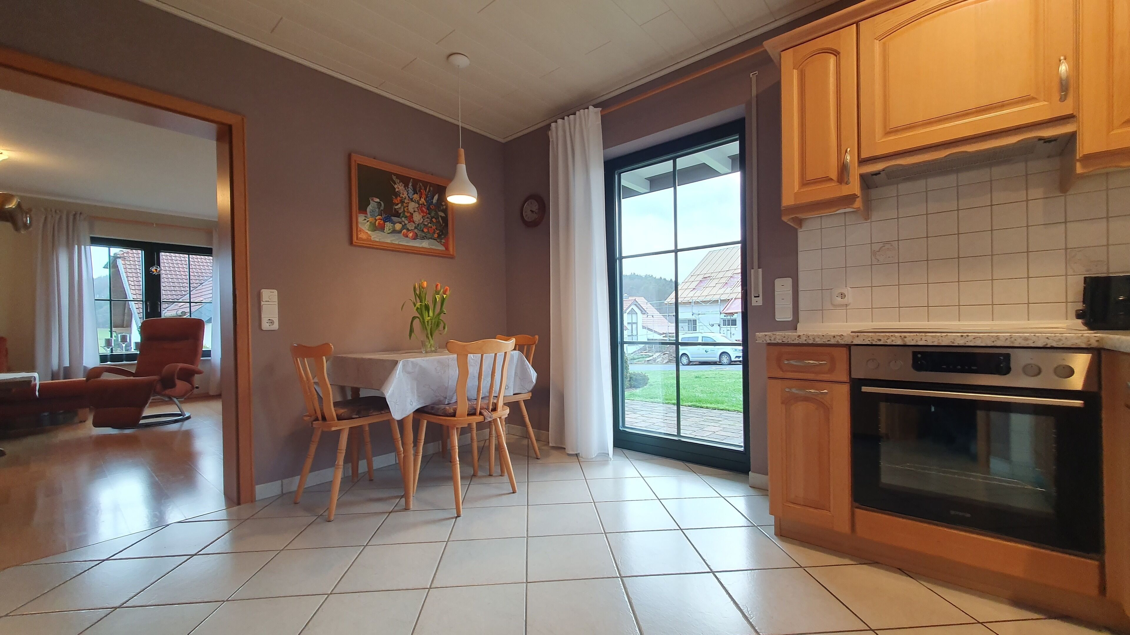 A kitchen with wooden cabinets, a dining table with chairs, and a view of the outside through a large window.