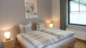 Ein Doppelbett mit karierter Bettwäsche, ein Nachttisch mit Lampe und ein Fenster mit Vorhängen.