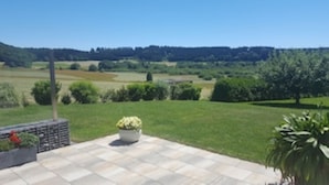 Eine Terrasse mit Blick auf einen Golfplatz und eine bewaldete Landschaft im Hintergrund.