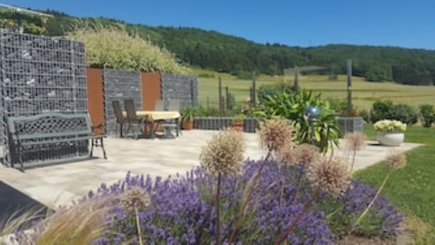Ein Patio im Freien mit Tisch und Stühlen, umgeben von einem Garten mit violetten Blumen.