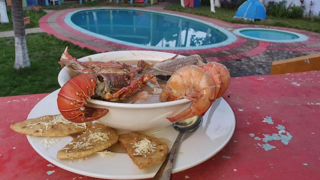 Un tavolo con una ciotola di frutti di mare, tra cui aragosta e gamberi, e del pane piatto su una tovaglia rossa.