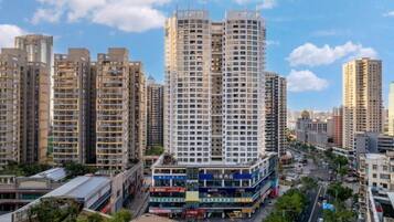 A high-rise residential building with multiple balconies, surrounded by other high-rise buildings, a street with vehicles, and a clear sky.
