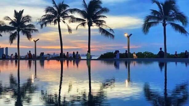 A serene waterfront scene with palm trees and a city skyline at dusk. - Chao Man Hotel, Haikou (Haikou)