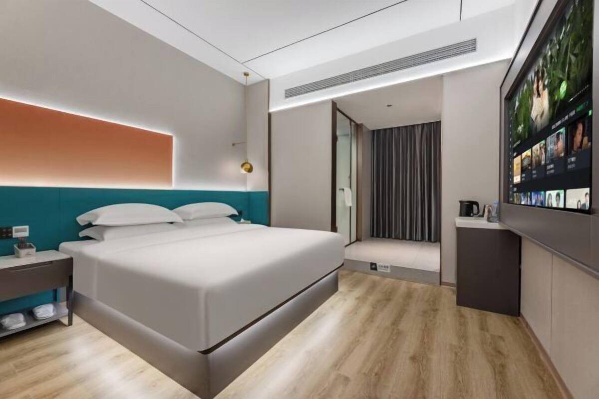 Une chambre d’hôtel moderne dotée d’un grand lit, d’une table de chevet, d’un téléviseur intégré et d’un coin salon agrémenté de rideaux.