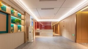 A modern hotel lobby with a reception desk, potted plants, and a clean, tiled floor. - Chao Man Hotel, Haikou (Haikou)