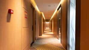 A hotel hallway with wooden walls, a patterned carpet, and a fire alarm on the left. - Chao Man Hotel, Haikou (Haikou)