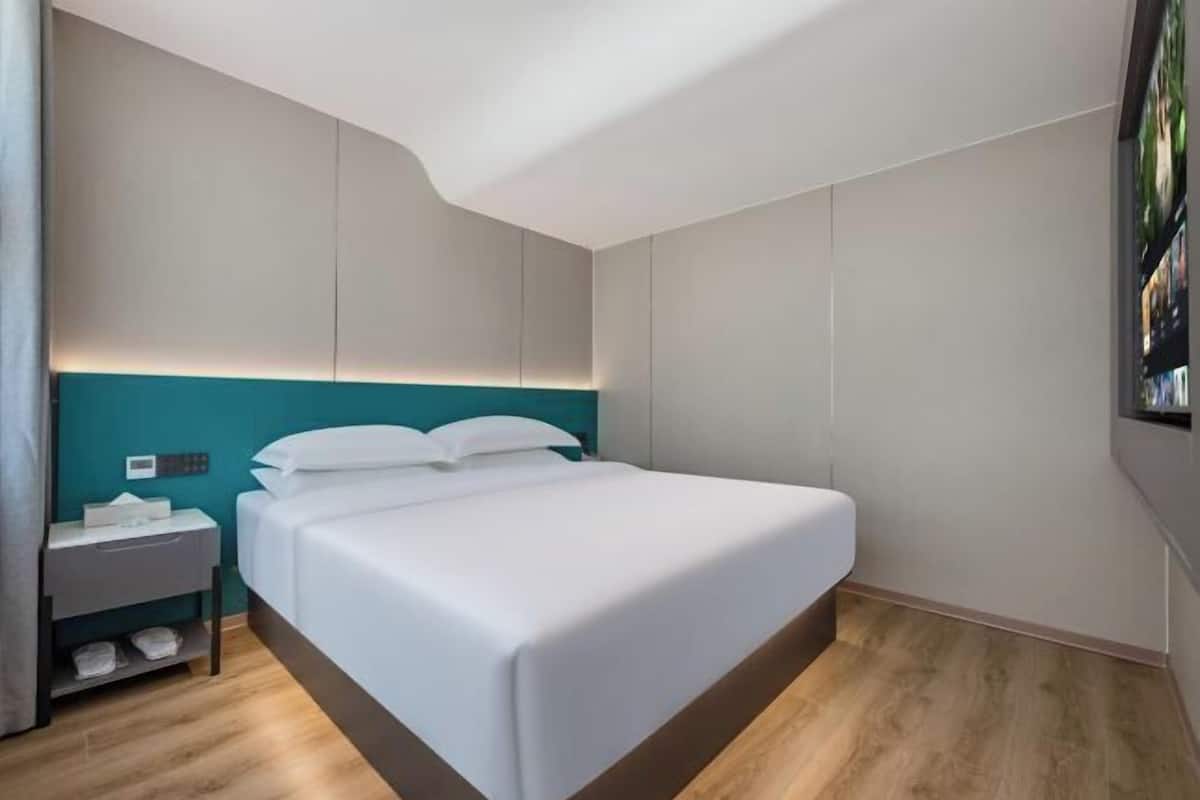 Une chambre d’hôtel moderne avec un lit soigneusement fait, une table de chevet avec une lampe et un panneau de commande fixé au mur.