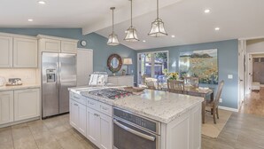 A modern kitchen with white cabinets, stainless steel appliances, and a large island with a built-in oven. - 3874 Mission Fields - Adorable Carmel Custom Home (Carmel)