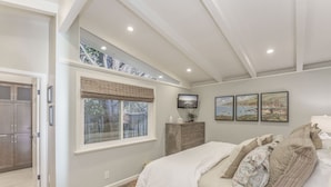 A bedroom with a large bed, a window with a view of trees, a dresser, and a television on the wall. - 3874 Mission Fields - Adorable Carmel Custom Home (Carmel)