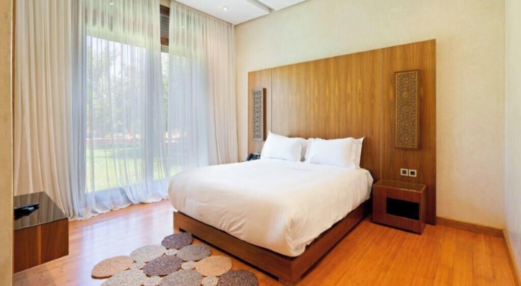 A modern bedroom with a wooden headboard, a large bed with white bedding, a bedside table, and a decorative rug.