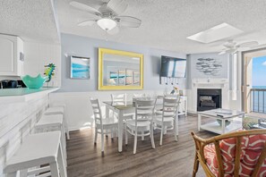 Un salon moderne comprenant un coin repas, des meubles blancs, une cheminée et une vue sur l’océan.