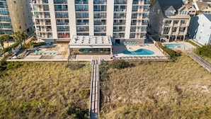Un hotel de gran altura con varios balcones, una piscina en la azotea y un paseo marítimo que conduce a una zona de playa.