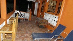 Ein Zimmer mit Fliesenboden, einem Holztisch mit Stühlen, einem blauen Sessel und einem Bett mit weißem Kopfteil.