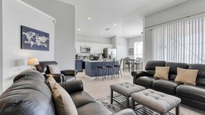 A modern living room with a leather sofa, a coffee table, and a dining area with a kitchen in the background. - Renovated 2023 - themed villa w/pool + game room (Kissimmee)