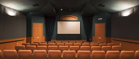 A movie theater with rows of orange seats, a large screen, and two doors with 'NO EXIT' signs.