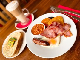 A breakfast plate with eggs, bacon, sausages, beans, toast, and a drink.
