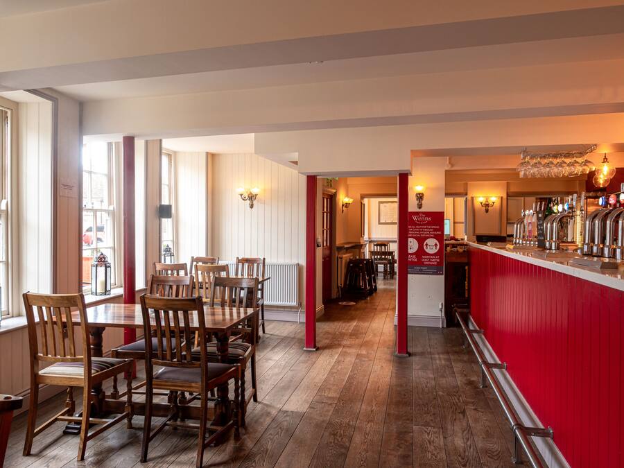 A restaurant interior with wooden tables and chairs, a bar area with a red counter, and a view of the street outside.