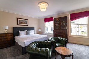 A hotel room with a large bed, two green leather armchairs, a wooden dresser, and a window with red curtains. - The Wenns Chop & Ale House (King's Lynn)