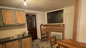 Et kompakt køkken med træskabe, et mønstret gulv, et spisebord med stole og en loftsvifte.