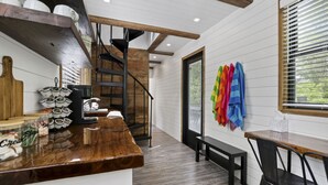 Une cuisine moderne avec un plan de travail en bois, un escalier en colimaçon et une vue sur la verdure à l’extérieur.