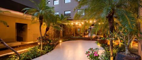 Un patio moderno de hotel con un camino curvo, palmeras y plantas en macetas.