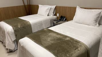 Two single beds with white linens and a brown accent, a wooden headboard, a telephone, and a small table.