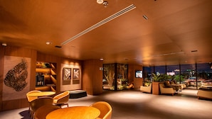 A modern interior with a wooden ceiling, a round table with chairs, a seating area with sofas, and a view through large windows. - Amazon Aeroporto Hotel (Varzea Grande)