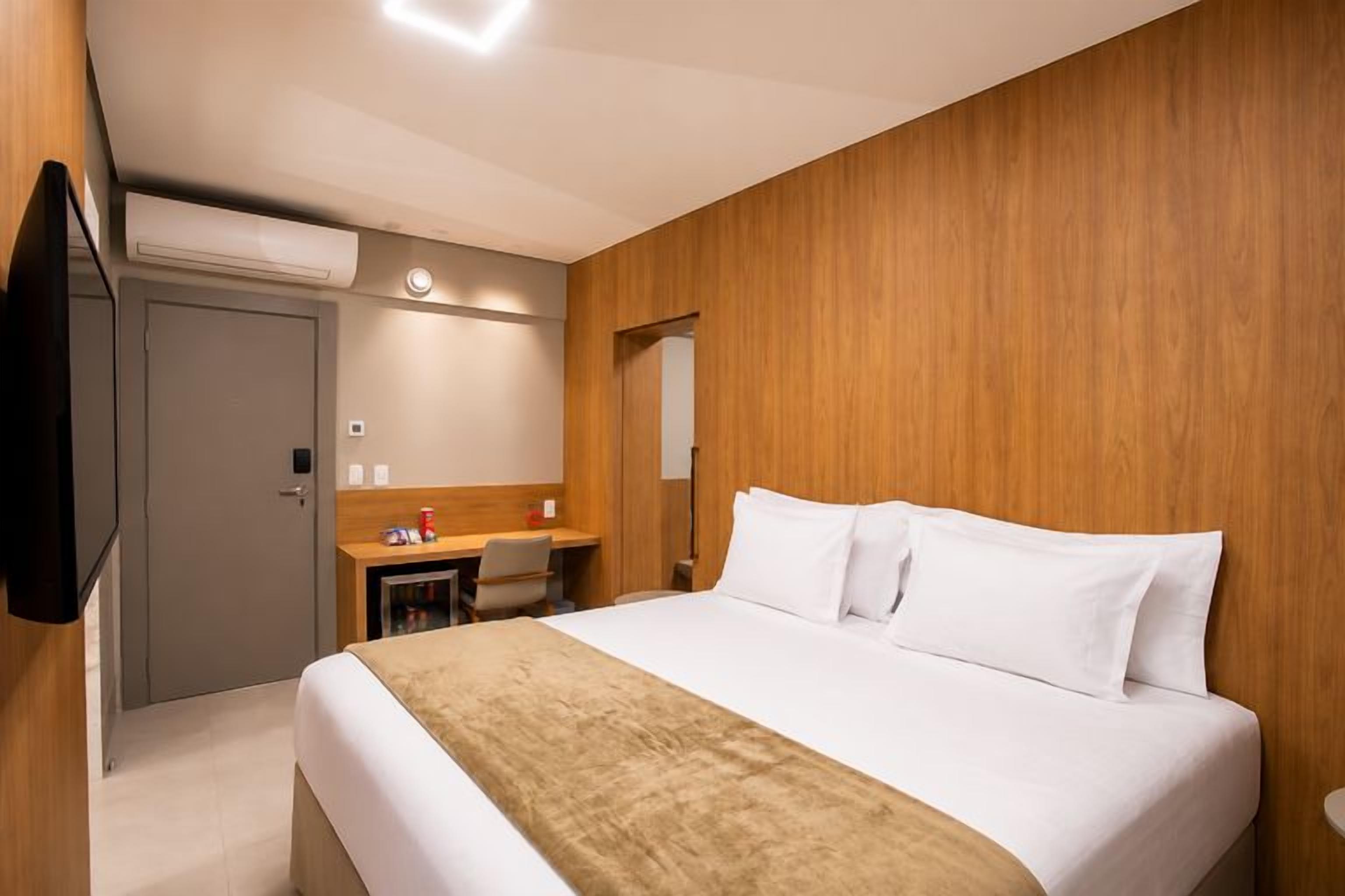 A hotel room with a bed, a desk, a chair, and a television.