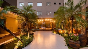 A hotel courtyard with a pool, palm trees, and a well-lit entrance. - Amazon Aeroporto Hotel (Varzea Grande)