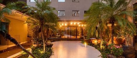 Patio de hotel con piscina, palmeras y una entrada bien iluminada.