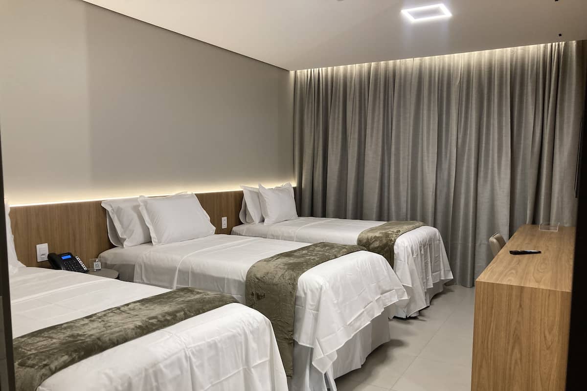 Quarto de hotel com duas camas, uma secretária de madeira, um telefone e uma cortina.