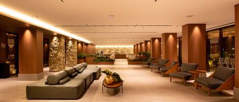 A spacious lobby with a modern design, featuring a seating area with sofas and armchairs, a central coffee table, and a stone accent wall.